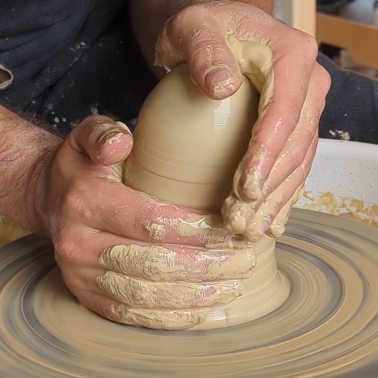 Person shaping a clay pot on a pottery wheel